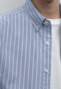 Jasnoniebieska koszula w paski z kołnierzykiem zapinanym na guziki, z wąskimi białymi paskami i białymi guzikami na gładkim materiale.