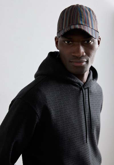 Svart huvtröja med texturerat mönster och snörning, ihopparad med en flerfärgad randig keps med en böjd skärm.