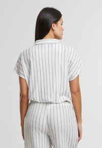 Top a righe bianche e nere con maniche corte, dal tocco morbido e un fit largo, dotato di colletto ed elastico in vita.