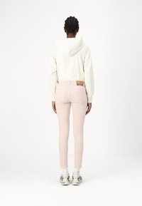 Sudadera beige claro con cremallera en la parte trasera y cordones blancos. Jeans rosa ajustados con dos bolsillos traseros y una etiqueta de tela en la cinturilla.