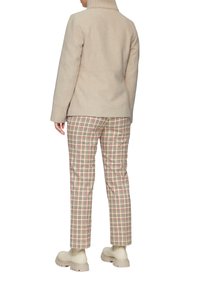 Beżowy płaszcz z mieszanki wełny z wysokim kołnierzem, zestawiony z beżowo-czerwonymi spodniami w kratkę. Obuwie to masywne beżowe buty.