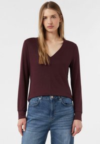 Bordeaux langelurig top met V-hals, gemaakt van zachte stof. Heeft een relaxte pasvorm, gecombineerd met blauwe denim jeans. Eenvoudig ontwerp en stikdetails.