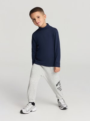 Dolcevita a maniche lunghe blu navy, abbinato a pantaloni jogger grigi con testo nero. Scarpe da ginnastica argentate con dettagli neri.