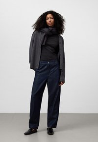 Grå knappad cardigan över en mörk topp, kombinerad med lösa, mörkblå denimbyxor och svarta slip-on skor. Mjuka texturer och avslappnad passform.