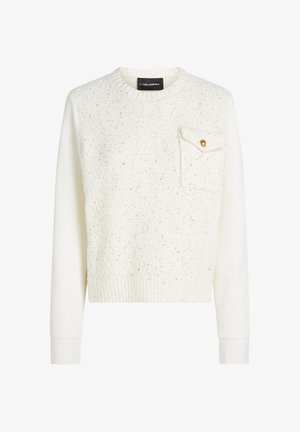 Valge pusa, millel on tekstuuriga kangas ja peene kuldse mustriga, ees tasku kuldse nupuga. Soonikkoes ääris ja varrukaotsad.