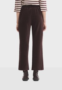 Woman wearing dark brown corduroy pants and dark leather ankle boots, standing against a plain white background.