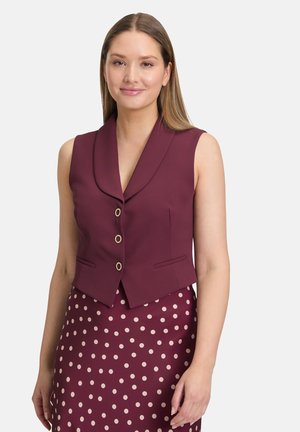 Gilet fitted senza maniche bordeaux con colletto a punte, tre bottoni dorati decorativi e due tasche laterali, abbinato a una gonna a pois.