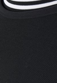 Gros plan sur un tissu noir texturé avec un col noir présentant une bande blanche le long du bord.