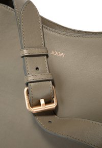 Sangle de sac en cuir vert olive avec une boucle ton or, présentant des coutures visibles et le logo embossé « JOOP ! » sur une surface lisse.