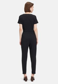 Giubbotto nero con maniche corte, vita stretta e gambe affusolate. Tessuto liscio e chiusura con zip sul retro. Tacchi in resina tartarugata.