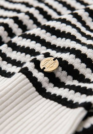 Jersey de punto a rayas negras y blancas con dobladillo acanalado y badge de logo dorado, que presenta líneas alternas gruesas y delgadas para añadir textura.