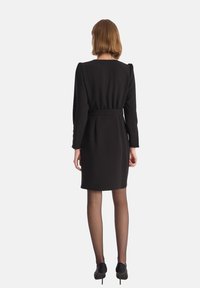 Czarna sukienka z długimi rękawami, dopasowanym wcięciem w talii i prostym krojem. Gładki materiał, minimalne detale szwowe i pasek na plecach.