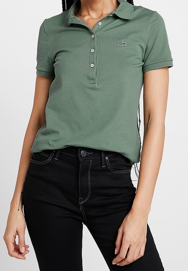 Personne portant un polo vert à manches courtes avec des boutons et un jean noir taille haute avec des coutures blanches.
