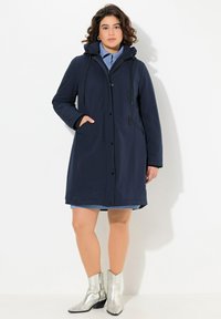 Navy blue hooded coat with a zip closure, side pockets, and drawstring. Features a sleek, smooth texture and knee-length design.