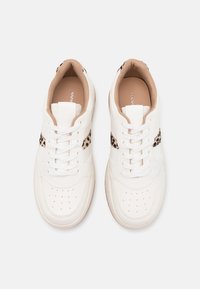 Baskets en cuir blanc avec un bout perforé, dotées d'un panneau beige avec des accents léopard sur les côtés et de lacets blancs.