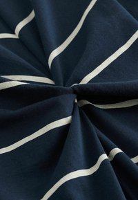 Marinblått tyg med horisontella vita ränder, som har en slät textur och lätt stretch. Tvinnat för detalj i en överlappande design.