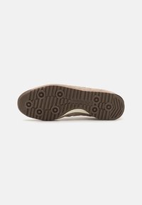 Suela de zapato de goma marrón con un diseño texturizado, que presenta agarres circulares y un logo de Adidas, diseñada para mejorar la tracción y la durabilidad.