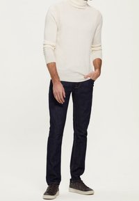 Cream turtleneck sweater, ribbed texture, dark blue slim-fit jeans, and brown sneakers with textured detail.