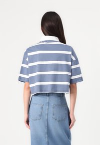 Camisola polo corta às riscas azul e branca com colarinho, combinada com uma saia de ganga azul de cintura alta com bolsos traseiros.