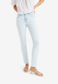 Světle modré skinny džíny vyrobené z denimu, s klasickým střihem a jemně bledým efektem. V kombinaci s bílými páskovými sandály.