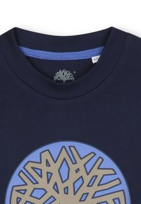 Granatowa bawełniana koszulka z okrągłym dekoltem. Na środku znajduje się duży niebiesko-beżowy wzór drzewa. Gładka tekstura i luźny fason.