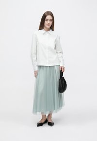 White fitted shirt with a collar, paired with a knee-length, light blue tulle skirt. Black handbag and black flats complete the look.