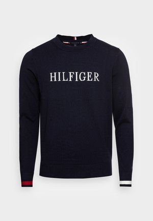 Granatowy sweter z długim rękawem z napisem "HILFIGER" na piersi w białym kolorze; czerwono-białe paski na mankietach rękawów.