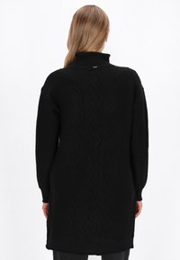 Czarny długi sweter z wysokim kołnierzem, z teksturowanymi wzorami z tyłu i ściągaczami na mankietach. Zaprojektowany z luźnym krojem, sięgającym do połowy uda.