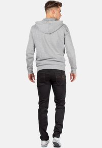 Haut à capuche gris avec cordon de serrage, associé à un jean noir avec poches arrière et détails de couture ; porté avec des baskets blanches.