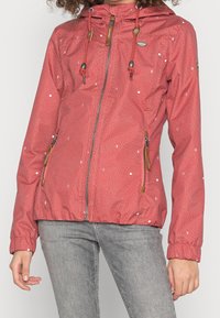 Red nylon jacket featuring a zip front, adjustable hood, and drawstring. Decorated with white polka dots and wooden accents on the zippers.
