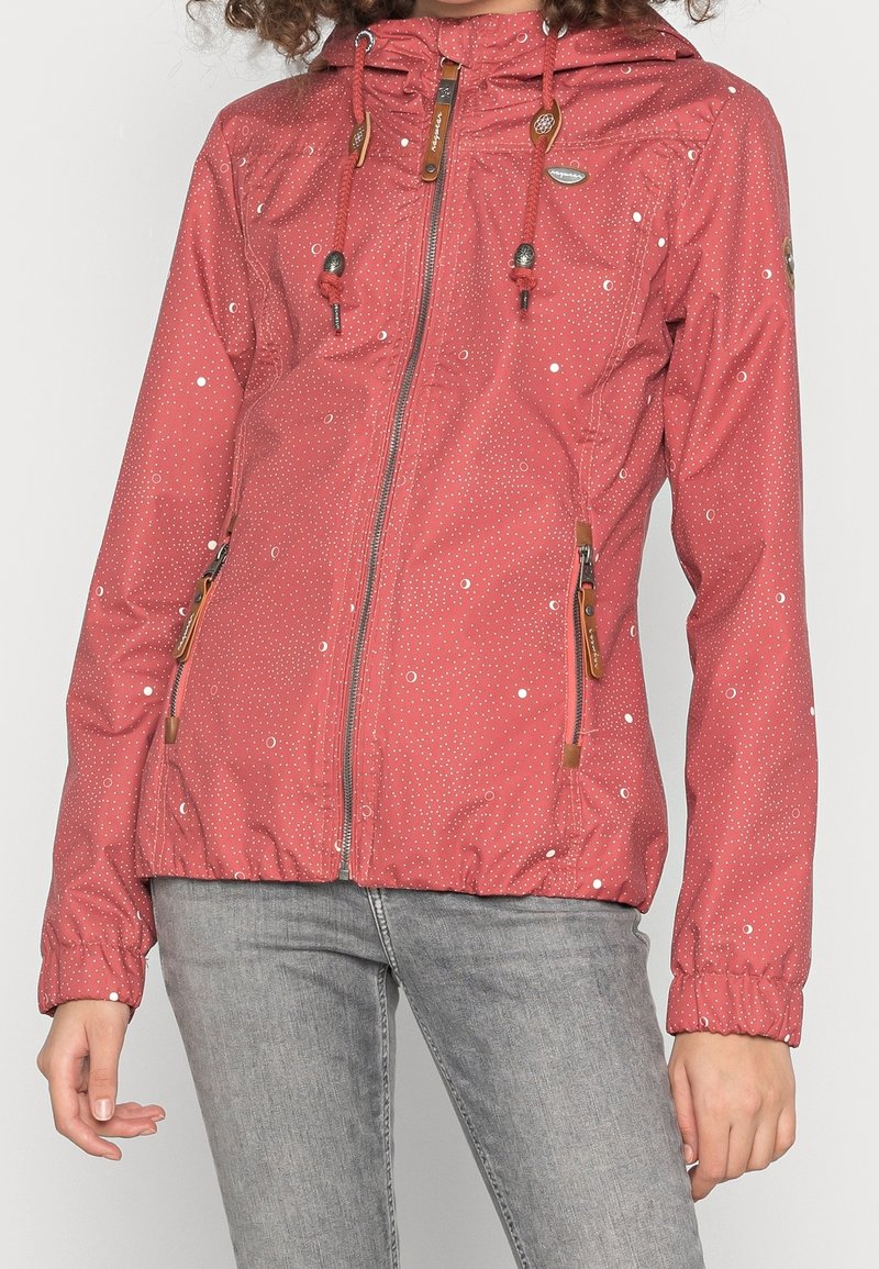 Red nylon jacket featuring a zip front, adjustable hood, and drawstring. Decorated with white polka dots and wooden accents on the zippers.