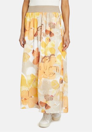 Blumenmaxiröhre mit einem beigefarbenen elastischen Bund, mit großen gelben und orangefarbenen Blütenmustern auf einem hellen Hintergrund. Getragen mit weißen Sneakers.