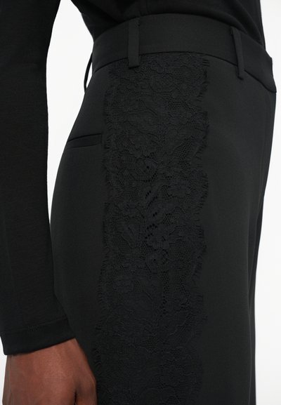 Čierne nohavice na mieru s textúrovaným čipkovým panelom po boku, doplnené hladkým materiálom a slim fit strihom.