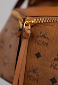Brun läderhandväska med präglat logomönster. Har guldfärgad dragkedja, matchande läderdetaljer och texturerad yta.