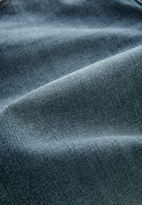 Țesătură denim de culoare albastru închis, cu o textură netedă, având cusături vizibile și variații subtile în culoare și modelul de țesătură.
