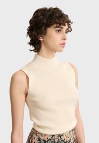 Geripptes, cremefarbenes, ärmelloses Oberteil mit hohem Ausschnitt, glatter Textur undFigurbetontem Design, kombiniert mit einem Rock mit Blumenmuster.