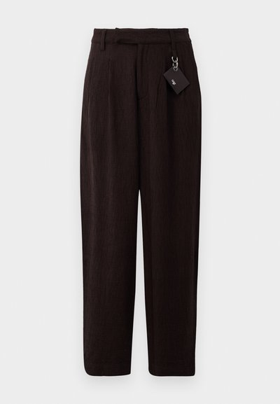 Pantaloni marroni scuri, strutturati, con una vestibilità ampia, caratterizzati da una vita con cintura e un'etichetta attaccata tramite un anello metallico. Davanti piatto e gambe dritte.
