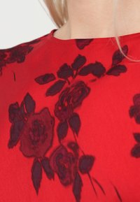 Rdeč pulover s cvetličnim vzorcem v temno bordo barvi. Tkanina ima gladko teksturo z enostavnim okroglim izrezom in kratkimi rokavi.