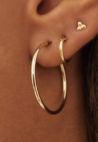 Gold hoop earrings with a shiny finish and smooth texture, paired with a small gold stud earring shaped like a cluster of three beads.
