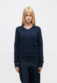 Kék sötétkék kardigán strukturált kötött anyagból, kerek nyakkivágással, gombos záródással és két elején masnis díszítésű zsebbel.