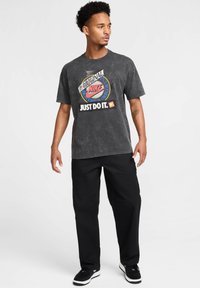 T-shirt grafica nera in jersey di cotone, con un logo Nike multicolore e scritte. Abbinato a pantaloni neri larghi e scarpe da ginnastica nere.