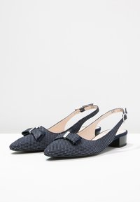 Zapatos de tacón slingback en color marino con puntera puntiaguda, patrón de lunares, detalle de lazo y tacón bajo tipo bloque. Fabricados en tela texturizada.