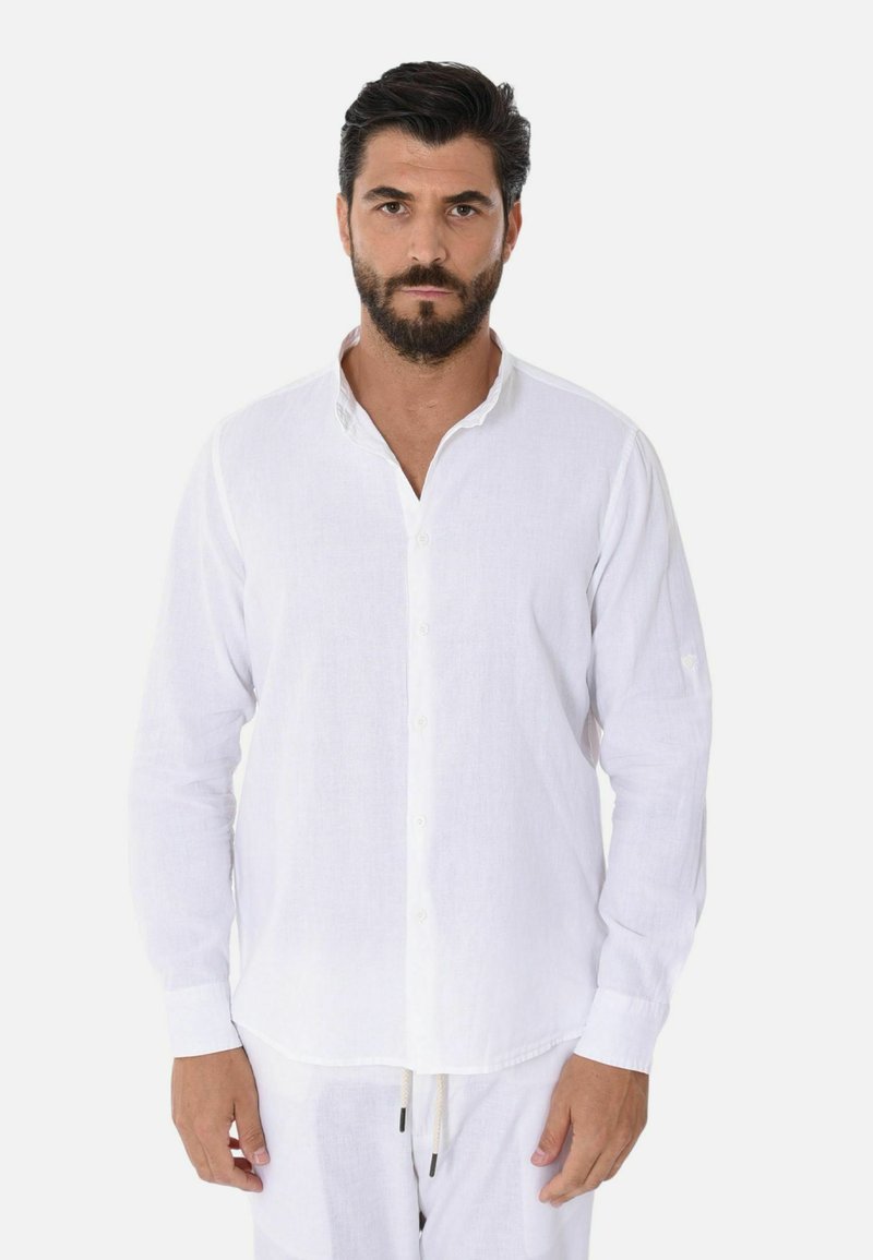 Camicia bianca a maniche lunghe in lino con colletto a V, chiusura a bottoni e una texture sottile, indossata con pantaloni chiari coordinati.