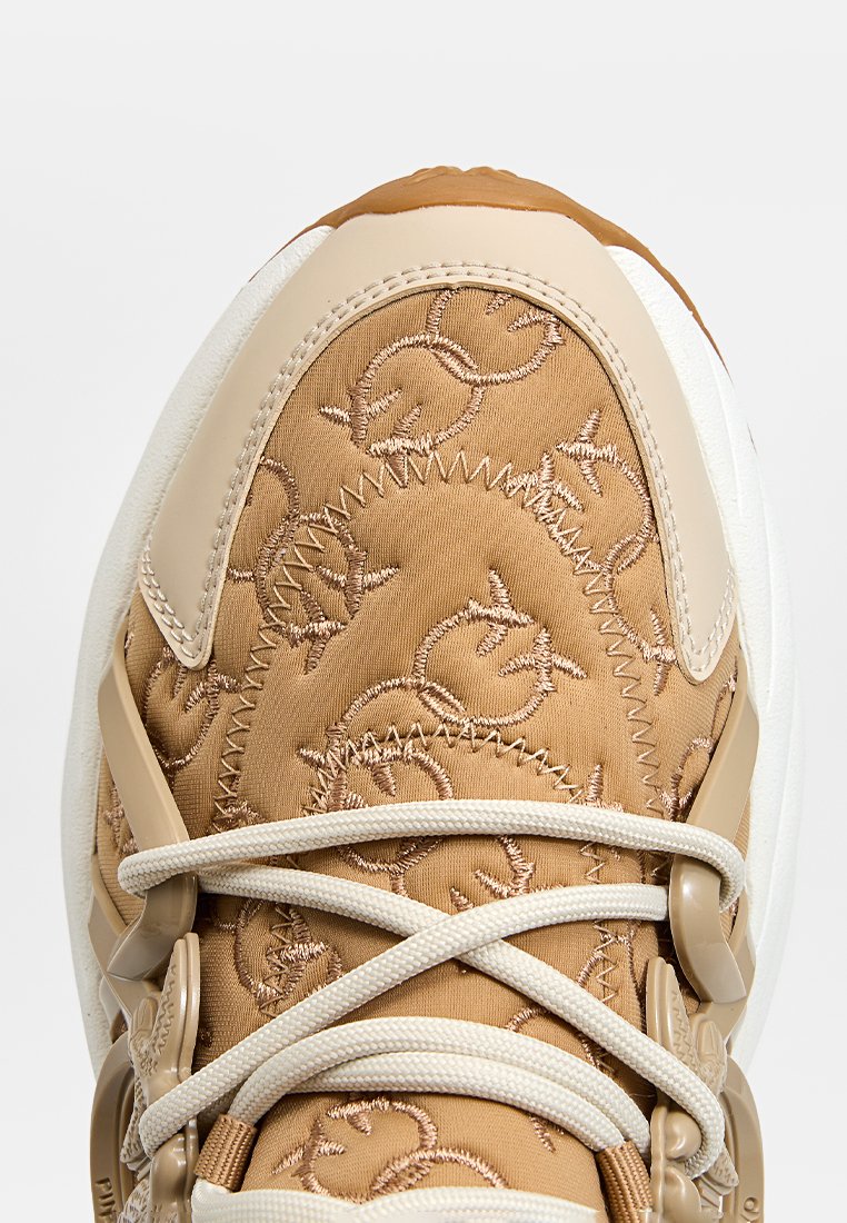 Baskets beige avec tige en tissu présentant des motifs en relief, semelle blanche épaisse et lacets beige contrastants fixés par des accessoires en plastique.