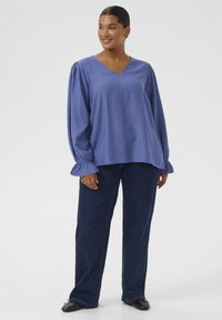Blue V-neck blouse with puffed long sleeves and ruffled cuffs, paired with dark blue denim pants. Smooth fabric texture with no patterns.