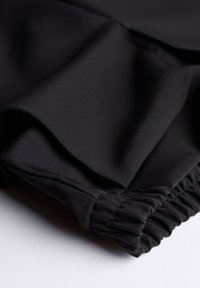 Pantaloni neri in tessuto morbido, con vita elastica e fondo arricciato. Design semplice, senza motivi o decorazioni.