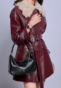 Cappotto in ecopelle bordeaux con colletto di pelliccia crema, vita con cintura e borsa nera con un accento a catena.