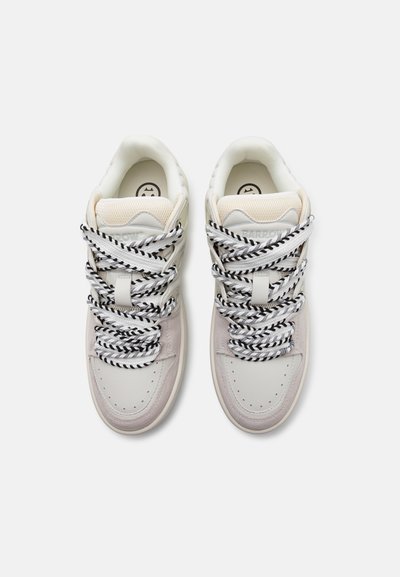 Sneakers con una toma superiore in pelle bianca e dettagli in suede grigio chiaro. Presentano lacci spessi a motivi neri e bianchi e una linguetta testurizzata.