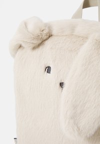 Furry beige backpack designed as a dog, featuring embroidered eyes, rounded ears, and textured fabric for a soft feel.