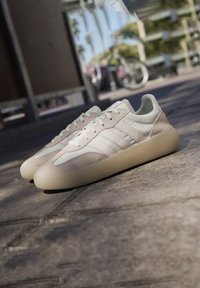 Beige sneakers med en slät läder- och mockaövre, rund tå, tre sidostripes och en kraftig beige gummisula.